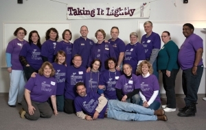 19 people posed beneath a banner that says 'Taking It Lightly'